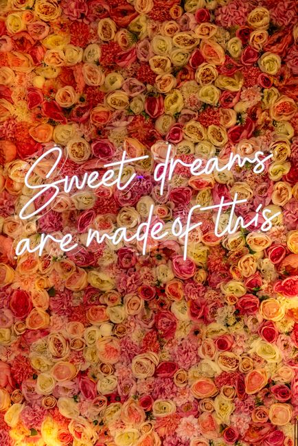 A dense arrangement of small, pastel-colored roses in shades of peach, pink, cream, and light yellow, creating a textured floral backdrop. The roses are tightly packed together, with visible green ste