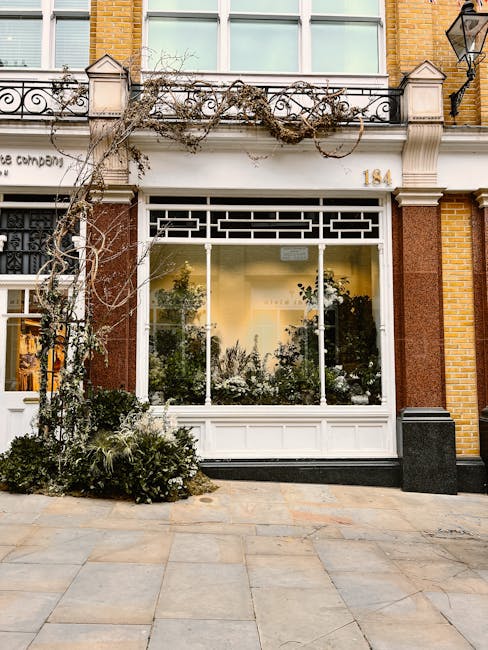 The image shows the exterior of a flower shop with large glass windows reflecting the interior and street scene. The shop's facade is decorated with a vine climbing the white-framed window, creating a