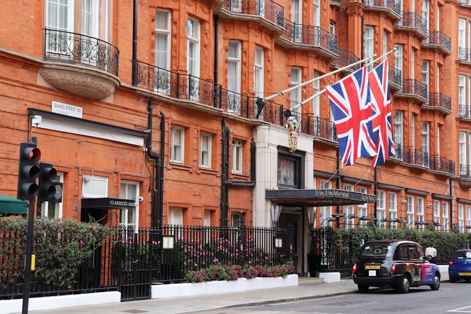 A view of a red-brick building on Davies Street W1, featuring balconies with black wrought-iron railings. Three large Union Jack flags are prominently displayed diagonally across the building’s faca