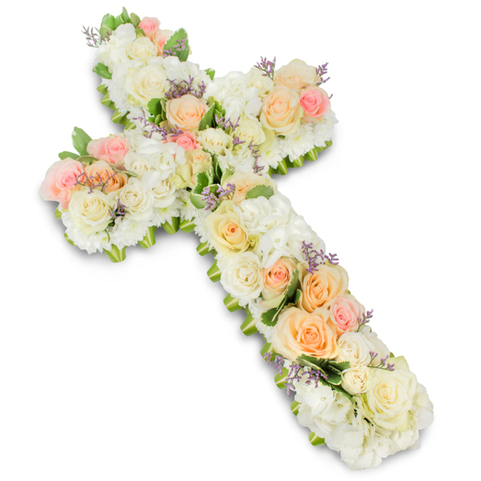 A meticulously arranged floral cross, designed as a heartfelt funeral or memorial tribute, is shown lying flat on a spotless white background, its entire surface covered with premium blooms in calm, pastel shades. The cross has softly rounded arms and a solid, reassuring shape, built from a rich base of ivory and white flowers including full roses, rounded hydrangea clusters, and compact spray roses that together create a plush, almost pillow-like effect. Nestled among these creamy tones are clusters of light peach, warm apricot, and delicate blush pink roses, arranged in gentle sweeps along the vertical and horizontal arms, guiding the eye through the design and adding a feeling of warmth and affection. Small, carefully placed hints of lavender or soft lilac filler flowers are tucked between the petals, introducing a whisper of colour that recalls the subtle elegance of Mayfair's garden squares and quiet courtyards. Fresh green foliage, trimmed and arranged with precision, edges the cross and peeks out from beneath the blooms, adding natural definition and depth while keeping the focus firmly on the flowers. The lighting is bright yet gentle, revealing the fine texture of each petal and casting a light shadow that gives the cross a sculpted, dimensional look against the white surface. Created with the kind of expertise you might expect from a long-established Mayfair florist, this floral cross embodies faith, solace, and remembrance, making it a fitting centrepiece for a church service, chapel farewell, or intimate gathering to celebrate a loved one's life with grace and quiet beauty.