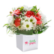 There's a gentle exuberance in this vibrant bouquet, carefully arranged in a pristine white square bag, as if it captures the spirit of a bright Mayfair morning. Lush coral and peach carnations, their signature ruffled petals full of plush texture, intermingle with crisp, white daisies crowned with lively lime-green centers, while airy baby's breath floats with whimsical grace throughout the display. A flourish of unopened, purple-tipped buds peeks beside the main flowers, introducing quiet depth and anticipation-echoing the secret gardens and tucked-away corners found just off Park Lane. Deep green, glossy leaves surround the bouquet, cocooning the arrangement with a sense of abundance and natural elegance as if shielding precious blooms from city bustle. The flowers are expertly styled to form a generous, rounded crown, speaking to the fresh artistry of a local Mayfair florist. Presented with sturdy, white ribbon handles, the bag feels both celebratory and practical-a perfect offering to brighten a friend's day in Mount Street, mark a new beginning near Berkeley Square, or surprise a loved one with the simple joy of fresh, seasonal blooms. With its immaculate white backdrop allowing each hue and form to shine, this bouquet feels like a personal moment of happiness plucked from the very heart of Mayfair.